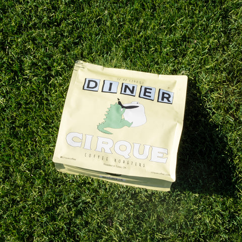 A package of Cirque coffee beans with the label 'Diner' placed on a grassy surface.