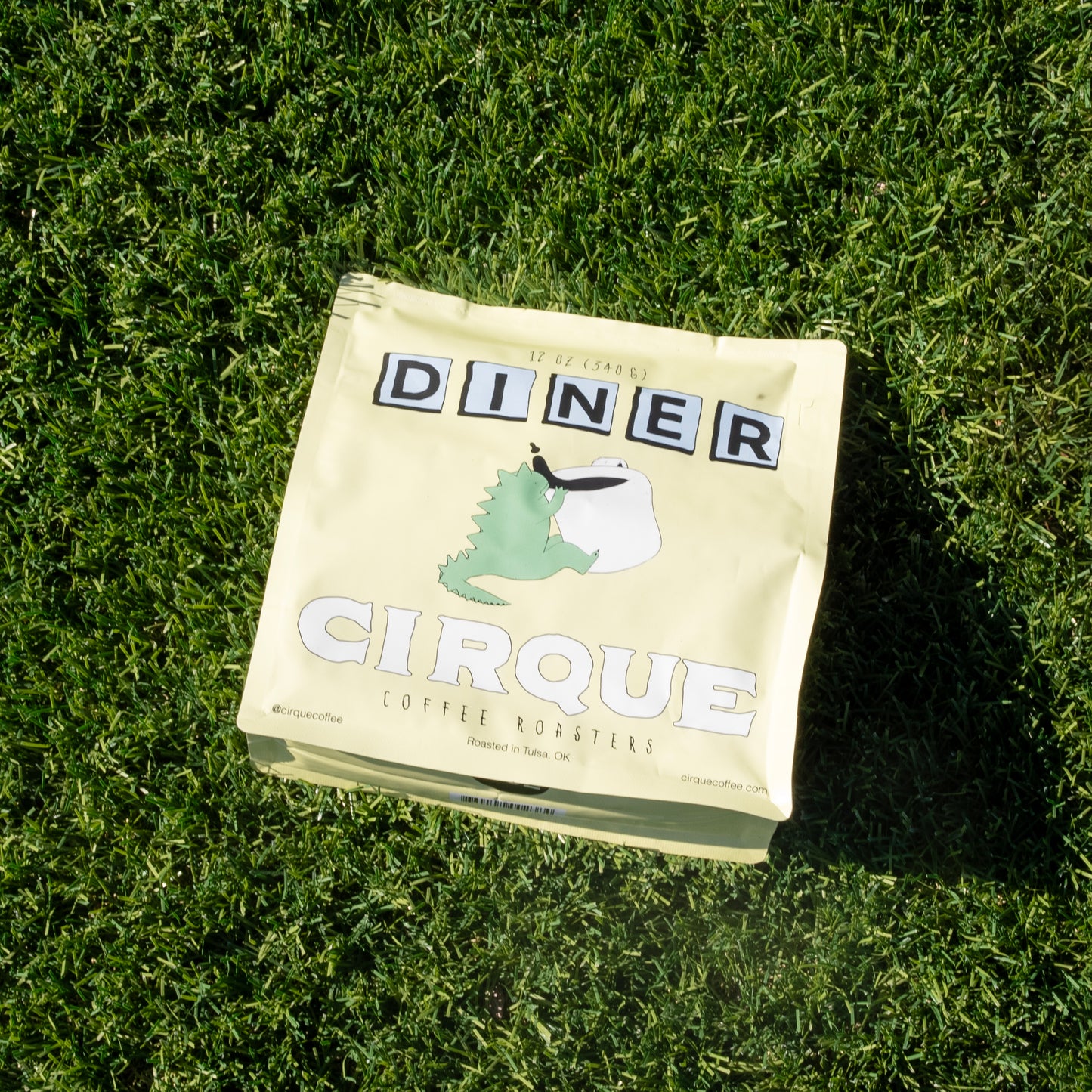 A package of Cirque coffee beans with the label 'Diner' placed on a grassy surface.